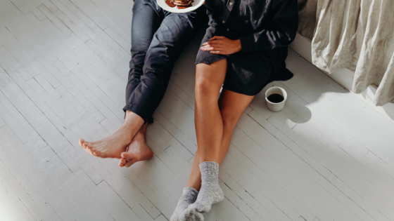 legs showing of 2 people sitting on the floor with coffee and breakfast