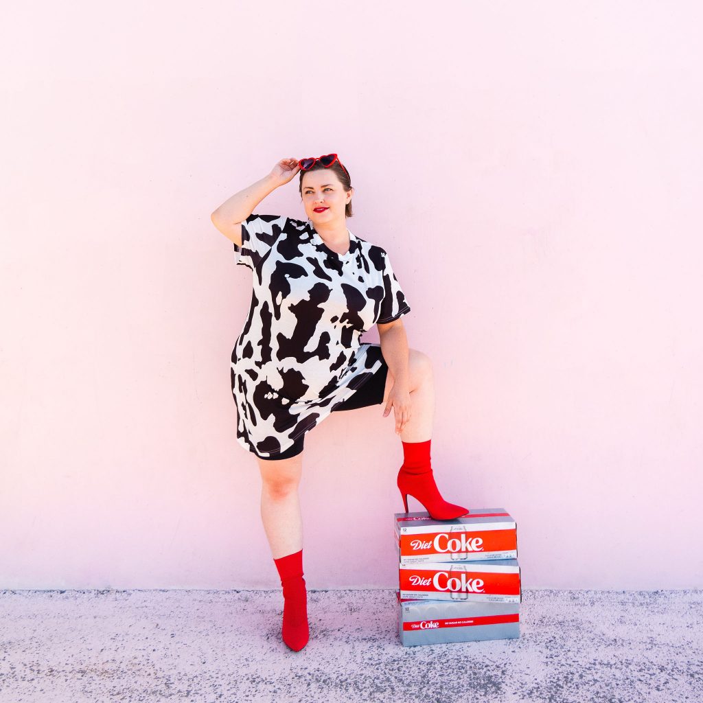 Snack blogger with diet coke and red heart sunglasses in cow print dress with red boots