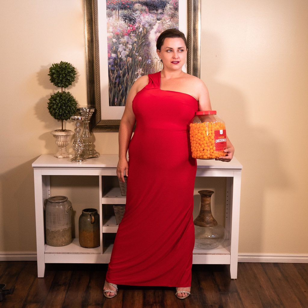 Fashion editorial photoshoot featuring cheese puffs as a snack.  Model in floor length red evening gown.