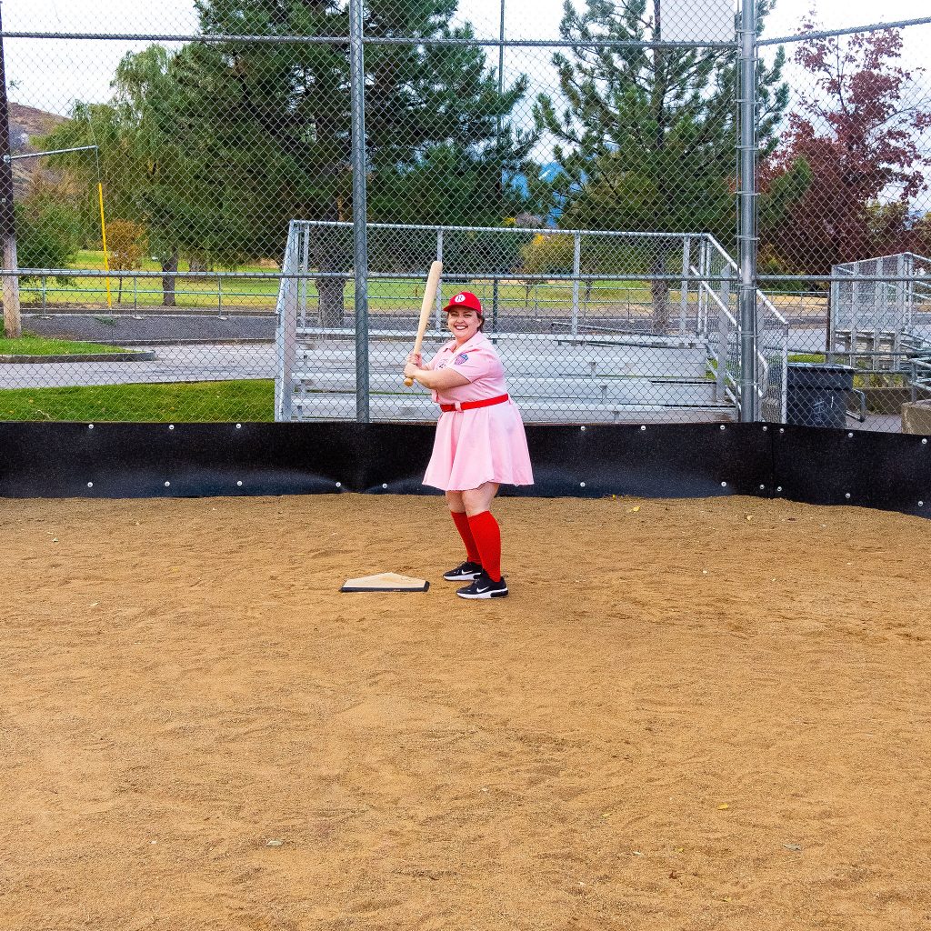 Costume Review - Plus Size a League of Their Own Halloween Costume - pink costume with blogger showing baseball hat on backwards and with baseball bat