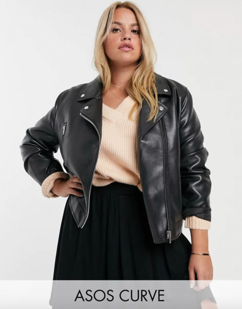 Black plus size moto jacket in faux leather. Blonde model in sweater and skirt and leather jacke