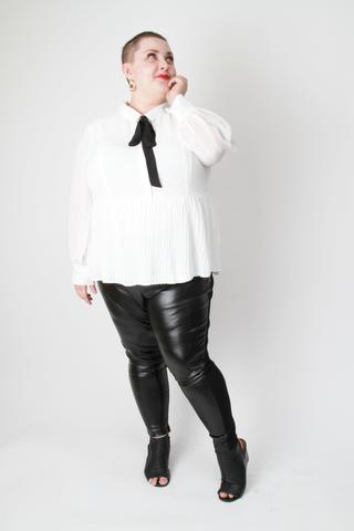 woman with shaved hair and round face with red lipstick in white top and black pants