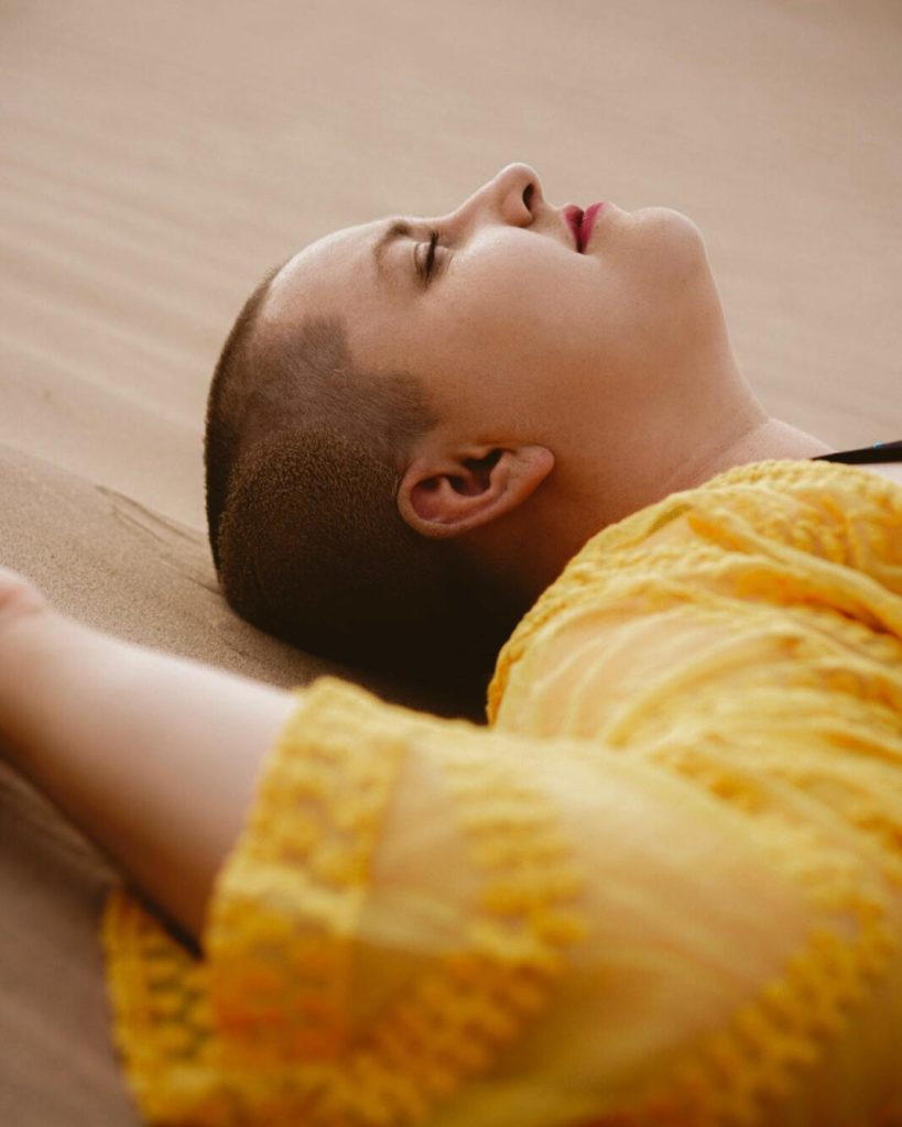 woman with shaved hair and round face with red lipstick in editorial photoshoot in desert