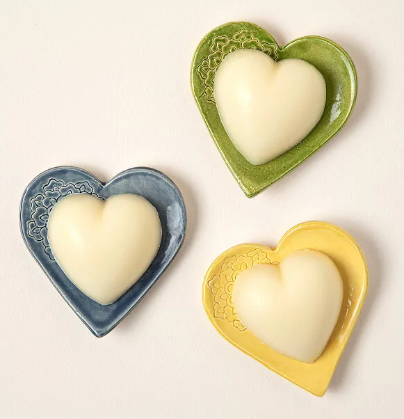 picture of 3 heart shaped dishes in green, blue and yellow with white heart shaped balm that looks like soap but it's actually lotion