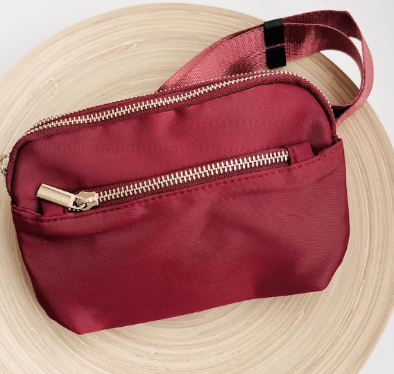 dark red shiny fanny pack with a zipper on the front in shiny dark red babric and gold hardware