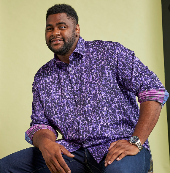 big and tall business casual outfit with a bright bold print purple shirt with contrasting cuffs rolled up. T he model is also wearing dark jeans.