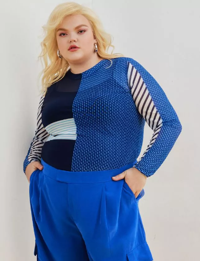 Plus size masculine androgynous clothing - model is wearing a bold blue mesh top with different patches of various patterns, as well as bright bold blue pants.